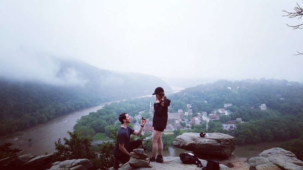 A man proposes to a woman on top of a cliff overlooking Harpers Ferry on a grey foggy morning.